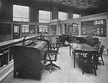Photograph of an office with several desks and a table with large windows in the background