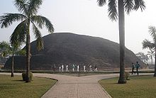 A very large hill behind two palm trees and a boulevard, where the Buddha is believed to have been cremated