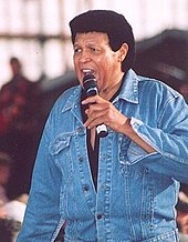 A color photograph of Chubby Checker standing with a microphone