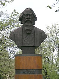 A cylindrical wood-trimmed plinth supports a bust of a bearded man in his sixties. On the plinth, a plate reads "Rabindranath Thakur".