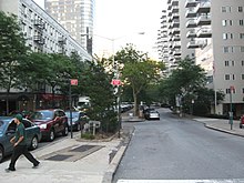 Looking east from Third Avenue along the median of 66th Street. There is a main roadway for through traffic on the left, as well as a service road for local traffic on the right. Manhattan House is on the right.