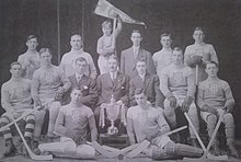 Black and white team photo with three rows of players surrounding the trophy