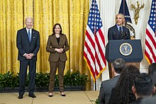 Obama speaking at a podium with President Biden and Vice President Harris standing beside him.