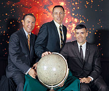 Three astronauts posing behind a lunar globe