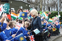 Camilla greets a group of schoolchildren holding the flags of the Commonwealth and various countries.