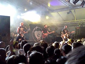 Rise Against performing on stage. Three band members can be seen, while the fourth is partially obscured.