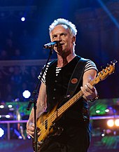 Sting playing guitar onstage.