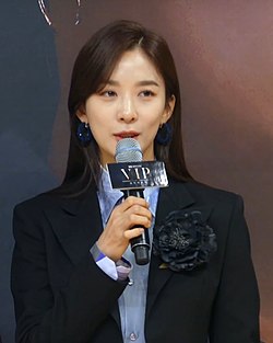 Lee wearing black suit and holding a mic in October 2019