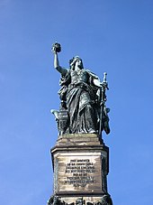 Споменик жени у одори која стоји, држећи круну у једној руци и мач у другој