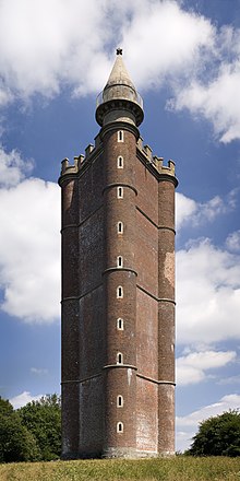 A brown triangular tower with curved corners, topped by a large finial.