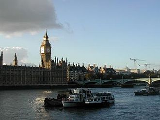 A large clock tower and other buildings line a great river.