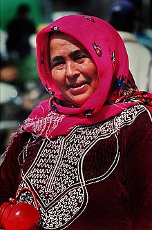 Smiling woman outdoors wearing a brightly coloured headscarf and embroidered clothing