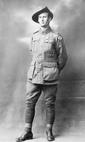 A full body portrait of a standing man. He is wearing a military uniform, a slouch hat and has a medal pinned to his left breast. His arms are behind his back and his right leg is forward. Three stripes can be seen on his right sleeve, denoting his rank as sergeant.