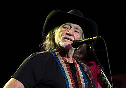 A man with long grey hair and a grey beard, wearing a black cowboy hat and black t-shirt