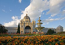Ornate white building with an elevated dome in the middle, fronted by a golden fountain and orange flowers