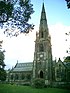 A Gothic style church dominated by a large, elaborate tower with a spire and pinnacles.