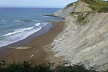 The ocean to the left, gentle tides coming in, a small piece of sandy beach before the white cliffs rise with grass on the top
