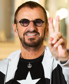 A colour photograph of Starr doing a peace sign wearing sunglasses and a black T-shirt