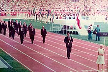 Athletes marching around a racing track then assembling on the inner green space of the stadium
