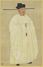 A man in heavy white robes, wearing a black hat with long horizontal protrusions coming from the bottom of the hat.