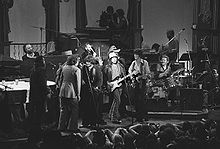 A black and white photo of about a dozen musicians performing on a stage.