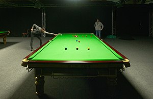 A player taking a shot at a practice snooker table, photographed from the opposite end of the table using a low camera angle to give forced perspective
