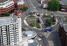 Aerial view of roundabout, a junction of several streets. Vehicles traverse around the roundabout, which is surrounded by buildings, mostly multi-storey