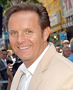 A man wearing a beige jacket with a white shirt, smiling and looking at camera