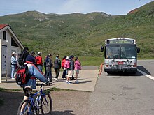 A bus in a parking lot, with grassy hills in the background