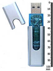 A USB thumb drive and its cap, next to a 100 millimeter ruler for scale