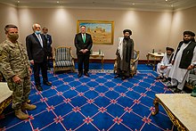 U.S. and Taliban officials stand spaced apart in a formal room