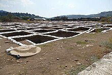an archaeological excavation at moza. General view of an area with a semi oblique perspective showing mostly square excavation trenches arranged in a checkerboard pattern in a mediterranean landscape.