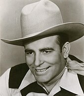 A smiling man wearing a cowboy hat and neckerchief