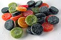 A pile of disk-shaped, sugar-coated, rubbery candies in red, green, orange, and mostly black