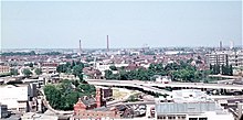 View from distance showing the ring road elevated highway and junction 2 in the middle distance with other buildings in the foreground and background, and several chimneys visible in the distance