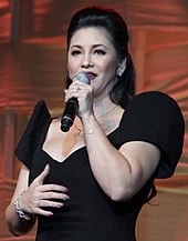 A photograph of woman wearing a black gown singing to a hand-held microphone