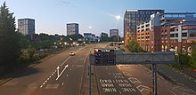 View of both carriageways and slip roads with a city centre car park on the right and tower blocks in the distance on the right