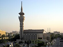The front side of a mosque with only one minaret containing a clock.