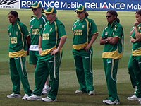 Six females in green cricketing outfits standing on the outfield looking at the presentation stage