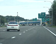 Ground-level view of four lanes of a busy freeway; several green exit signs and two overpass bridges are visible in the distance.