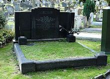 A large gravestone of black marble with a patch of green turf in the middle