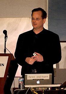 Lawrence Lessig standing at a podium with a microphone, with a laptop computer in front of him.