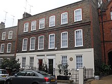 Two Georgian terraced houses in brown brick with the bottom storey in stucco, that on the right with a brown circular plaque marking Mozart's residence