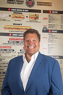 Headshot of Jimmy John Liautaud in 2018 in front of a Jimmy John's menu