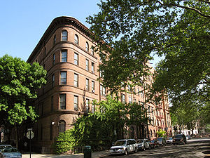 Brick townhouse along a street, which is lined with trees.