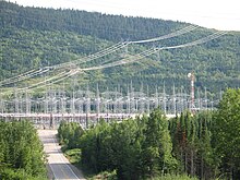 Power lines reach a hub in a densely forested area. A road going downhill leads to a forest of metal pylons.