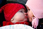 A young girl kisses a baby on the cheek.
