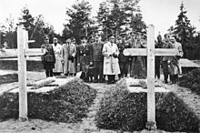17 người đàn ông, phần lớn trong quân phục, đứng trong một nghĩa trang, nhìn hai nấm mồ.
