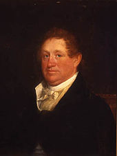 A red-haired man wearing a black jacket and white high-collared shirt
