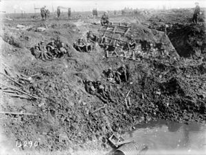 A black and white photograph of men in military uniform resting on the sloping sides of a large crater on a battlefield